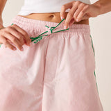 Person wearing pink shorts with green trim, adjusting the waistband against a neutral background.