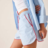 Person wearing light blue shorts with red trim and a light blue shirt on a neutral background