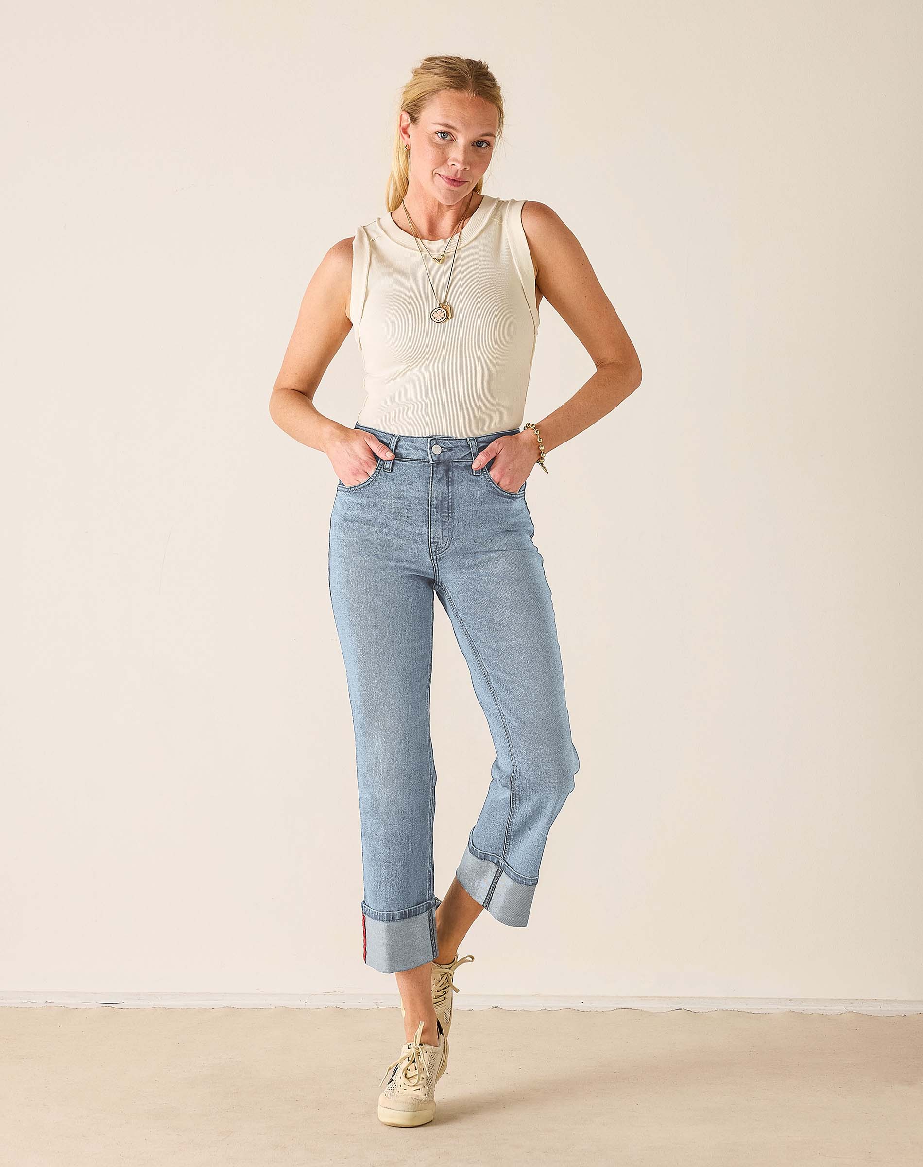 Woman wearing light blue jeans and a white sleeveless top against a plain background