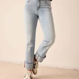 Person wearing light blue jeans and white sneakers on a beige floor with a neutral wall background