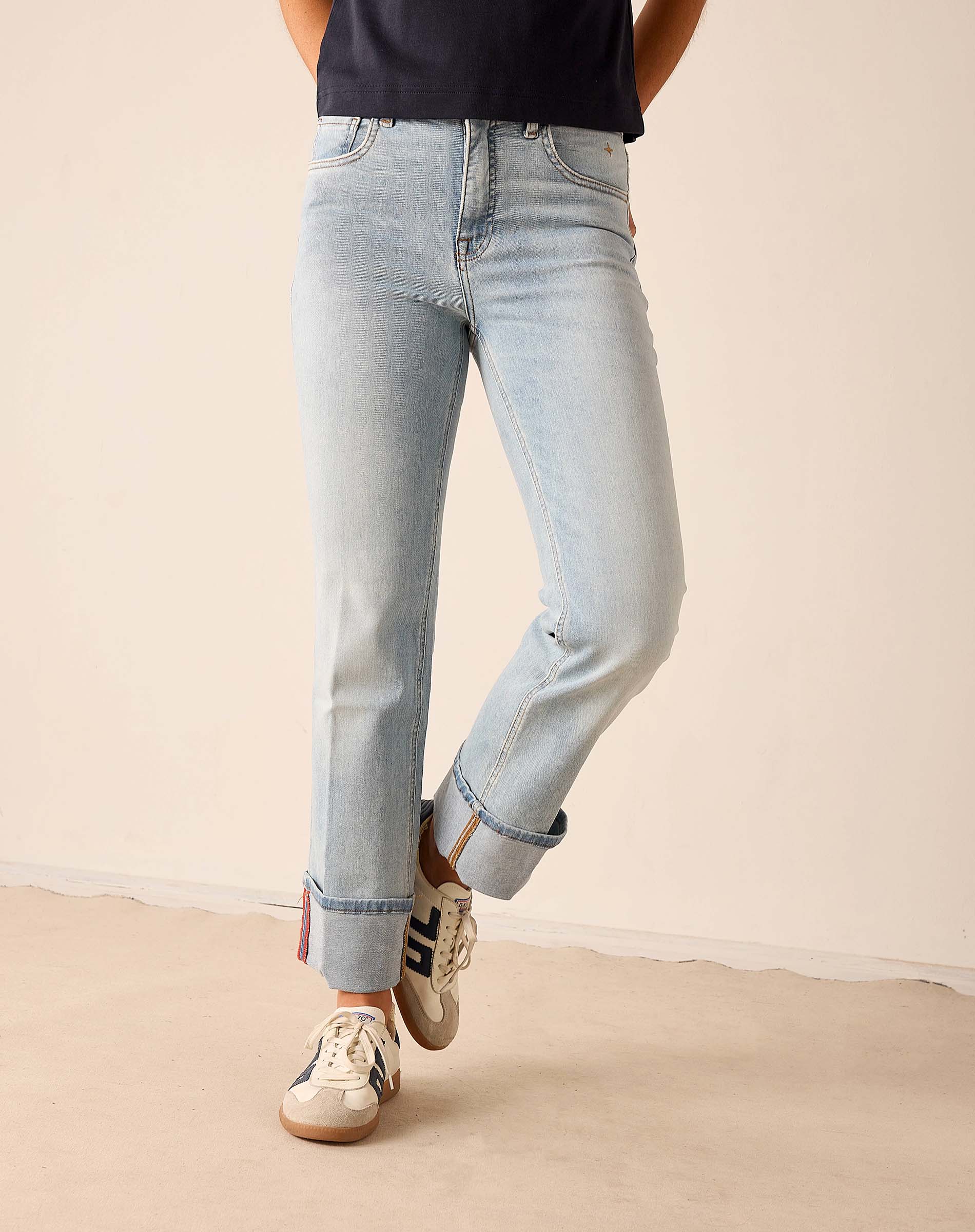 Person wearing light blue jeans and white sneakers on a beige floor with a neutral wall background