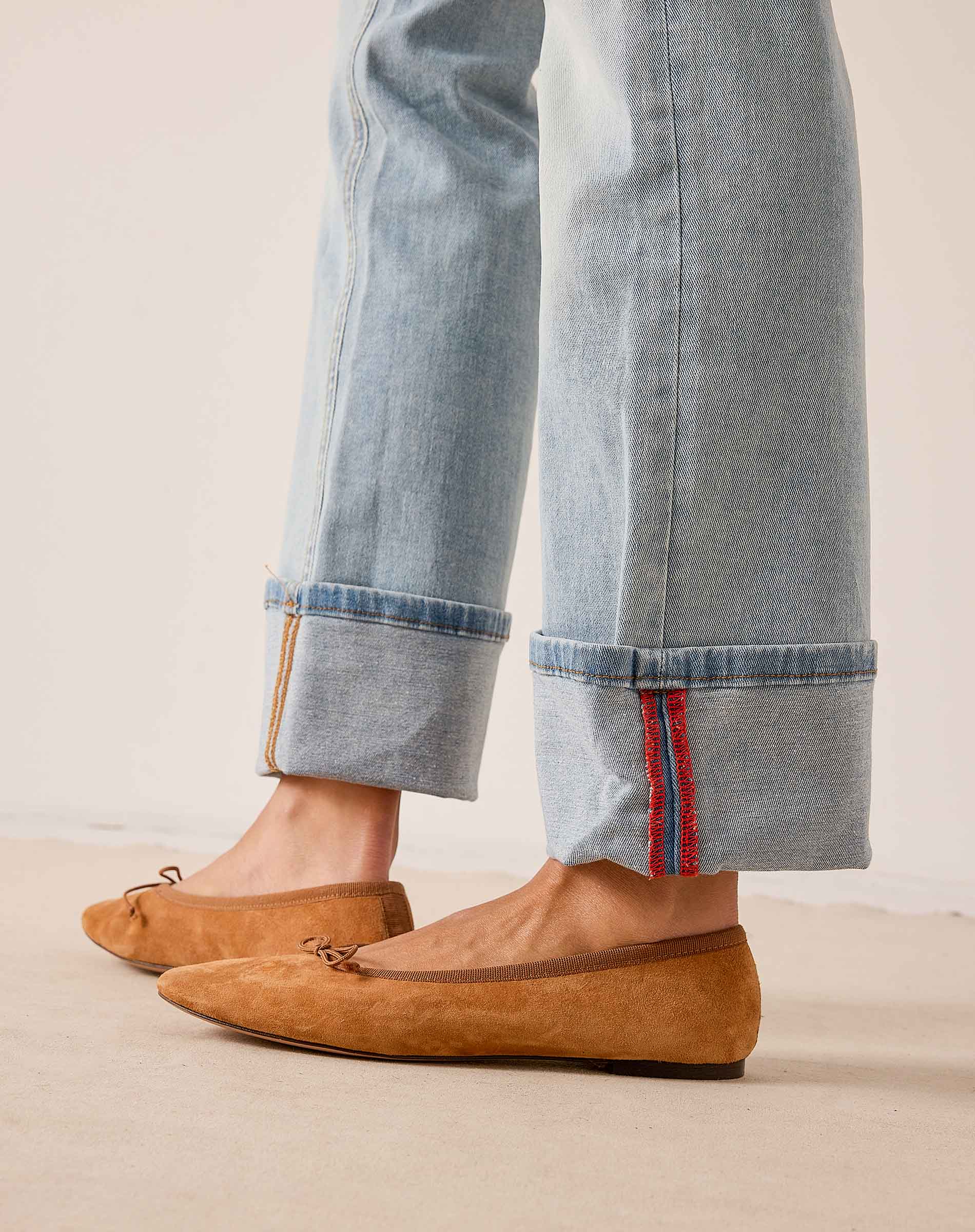 Light blue denim straight-leg pants with cuffed hems and contrast stitching, paired with mustard yellow suede loafers.