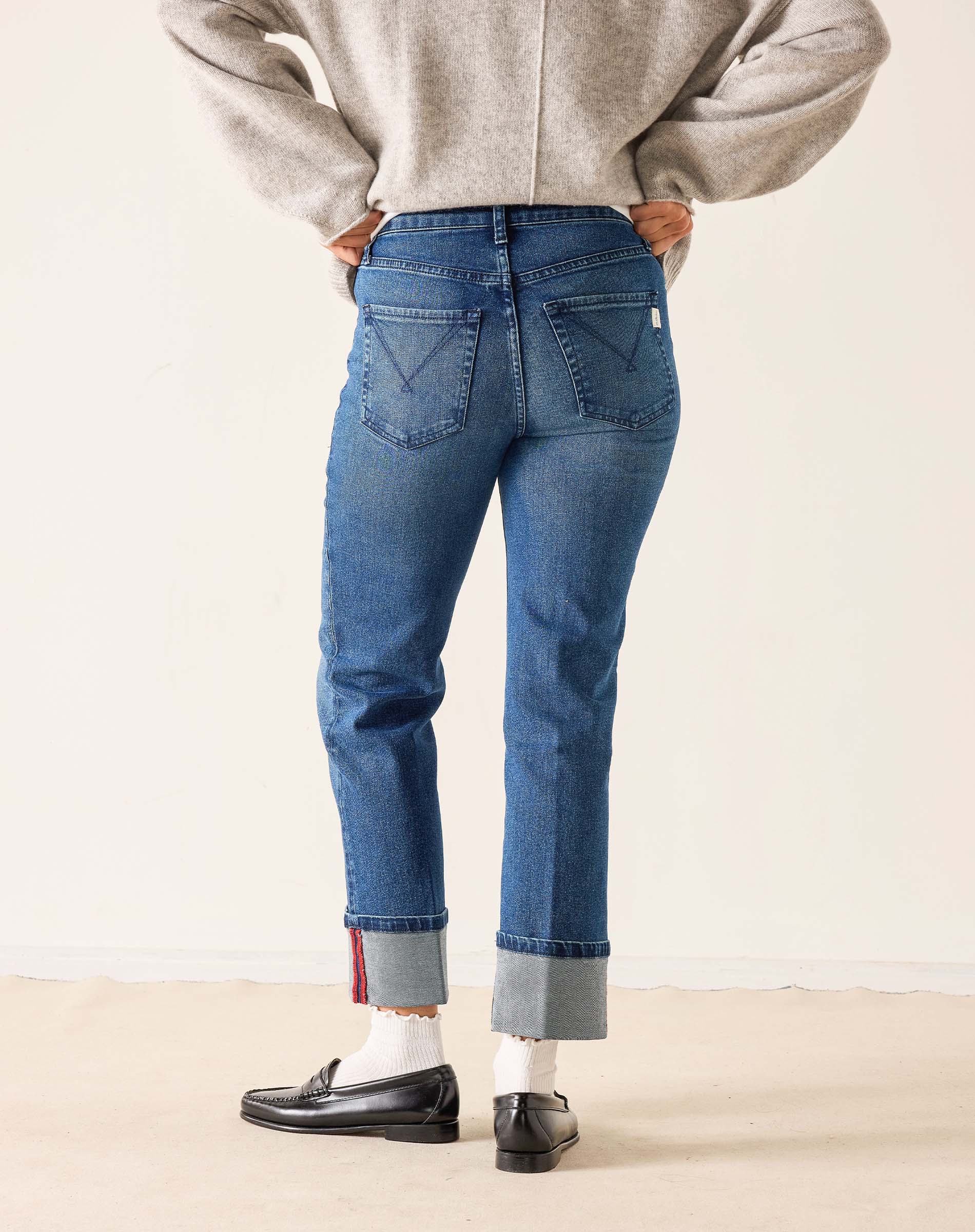 Person wearing blue jeans and a gray sweater on a plain background