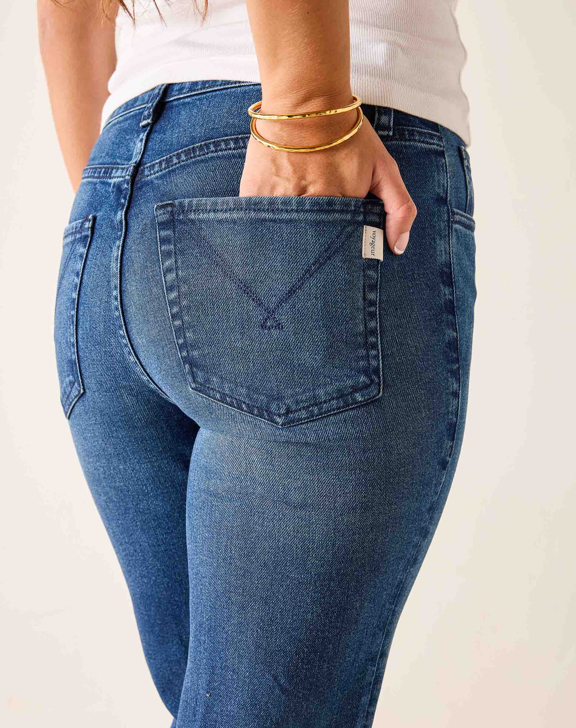 Person wearing blue jeans with a visible brand logo on a plain background