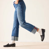 Person wearing blue jeans with rolled-up cuffs, white socks, and black shoes on a plain background