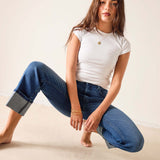 Woman wearing a white t-shirt and blue jeans sitting on a beige surface.