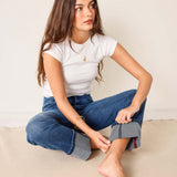Woman sitting on a beige surface wearing a white t-shirt and blue jeans.