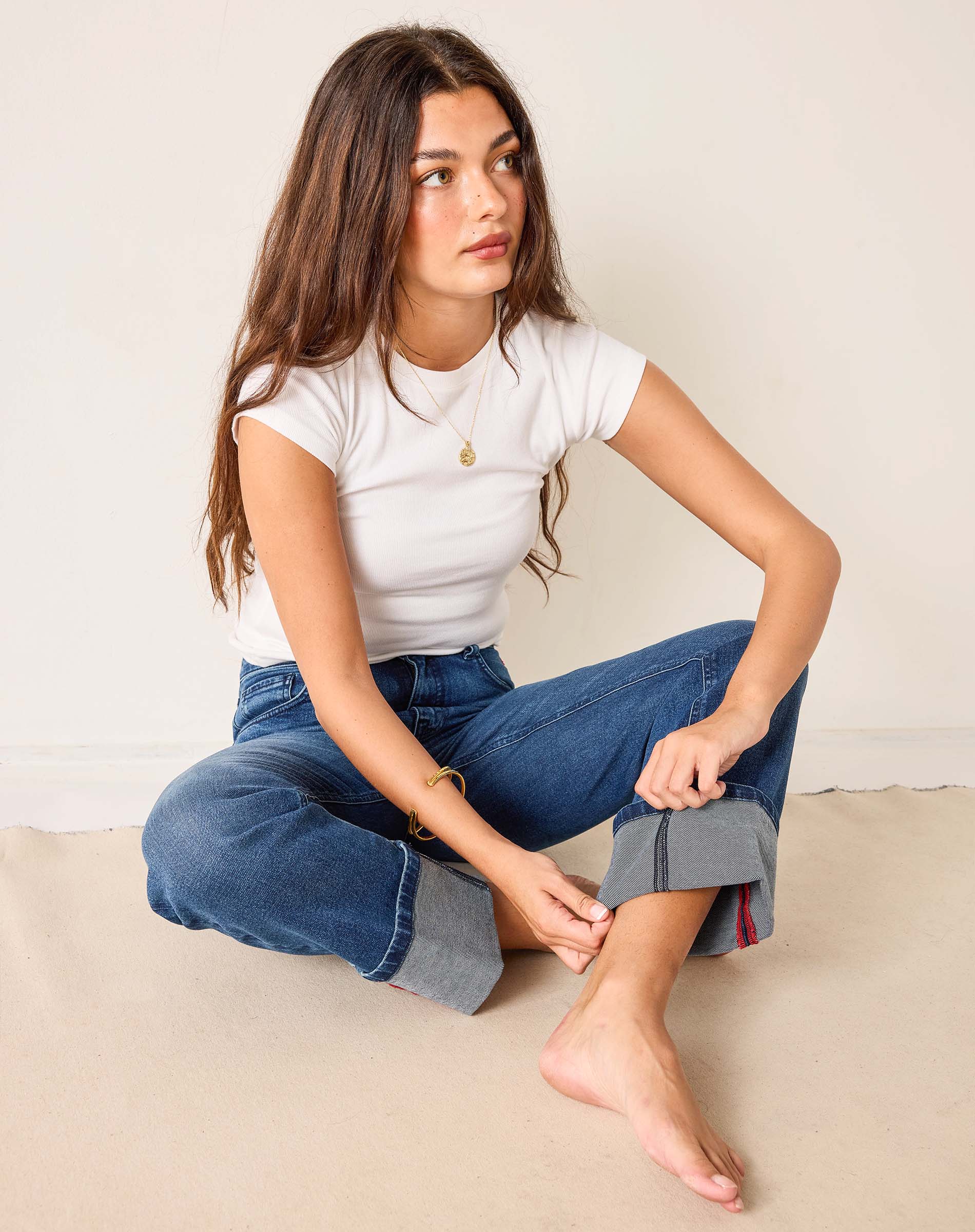 Woman sitting on a beige surface wearing a white t-shirt and blue jeans.