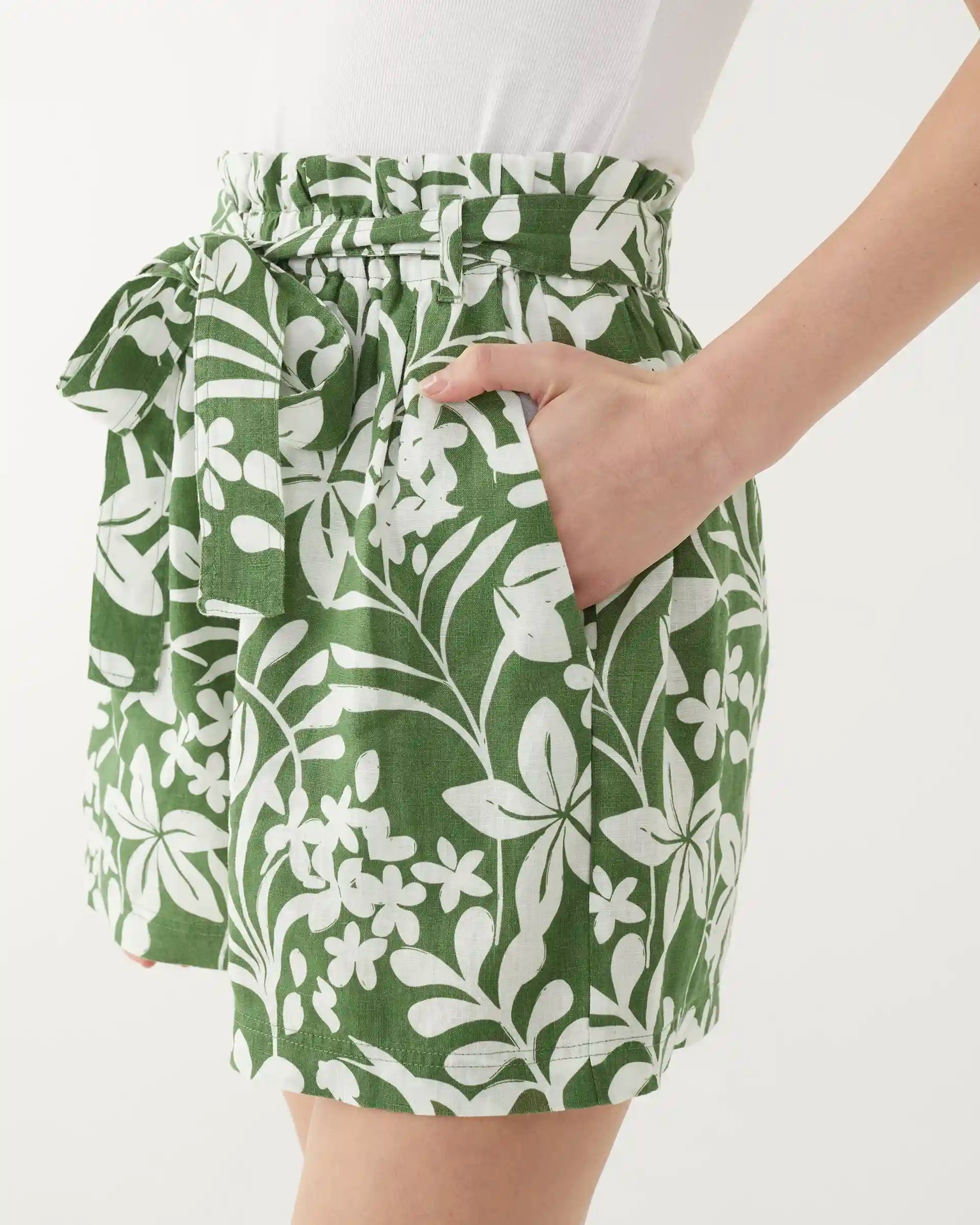 female wearing green shorts with white floral print and one hand in pocket on a white background