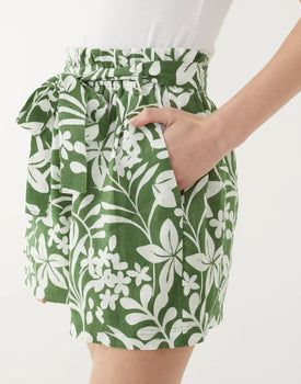 female wearing green shorts with white floral print and one hand in pocket on a white background