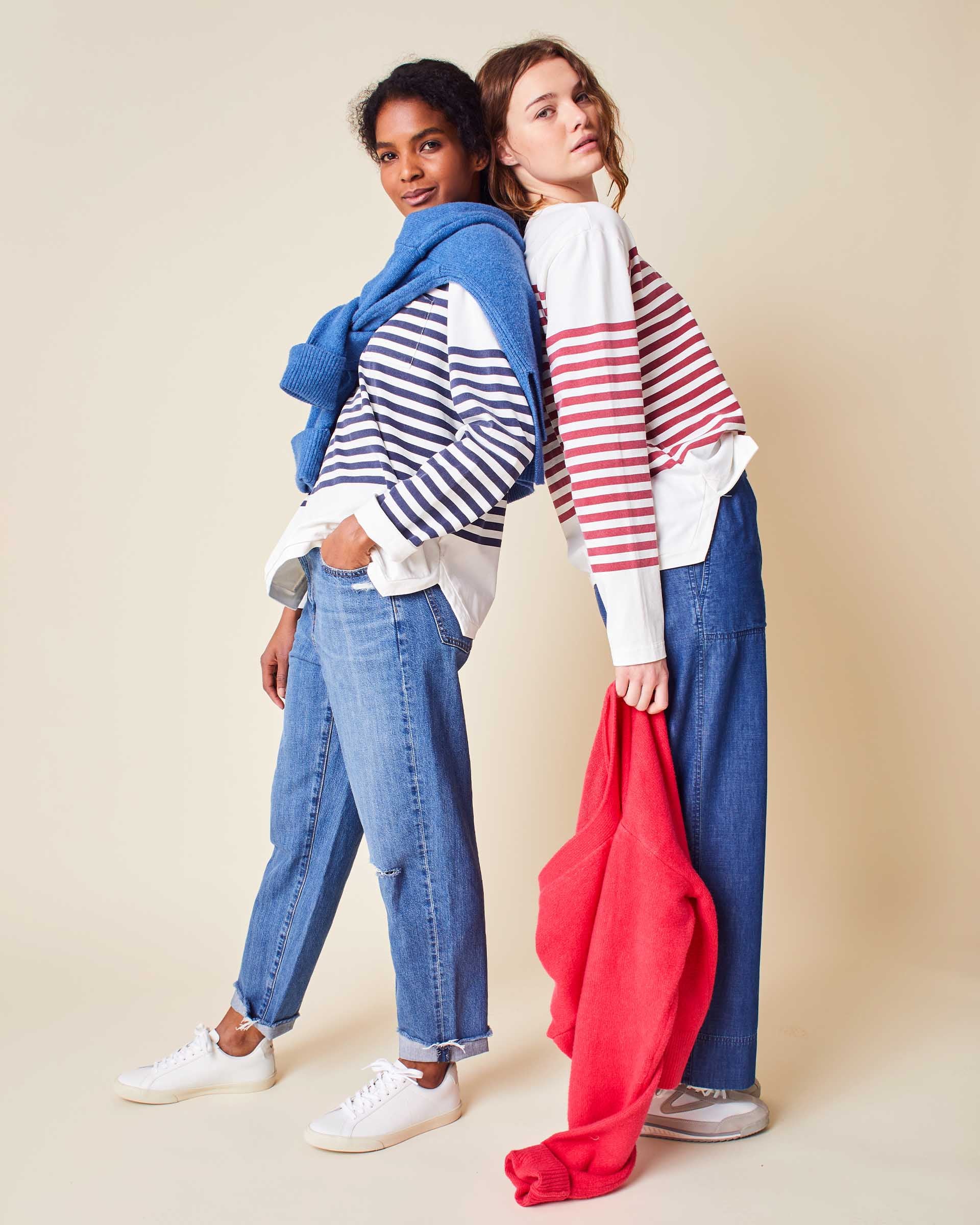 two women wearing mersea boater long sleeve tees in navy and red stripes leaning back to back