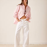 Woman wearing a pink blouse and white pants against a plain background