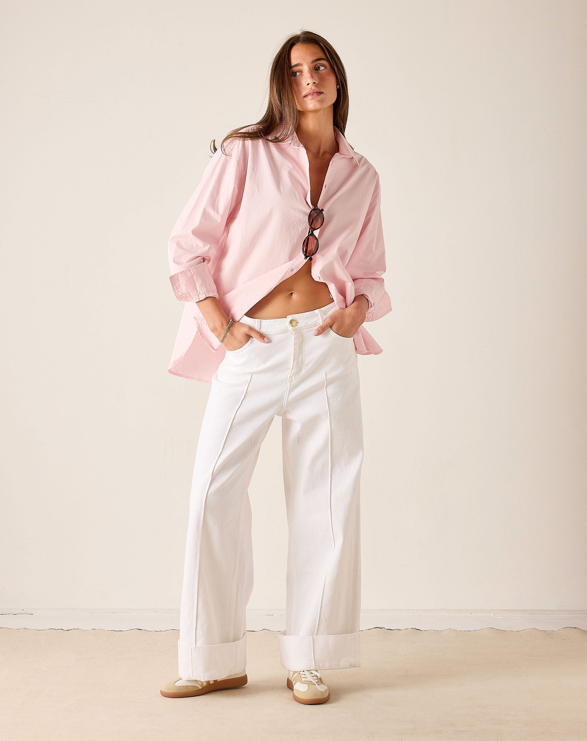 Woman wearing a pink blouse and white pants against a plain background