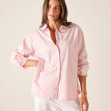 Woman wearing a light pink shirt and white pants against a plain background