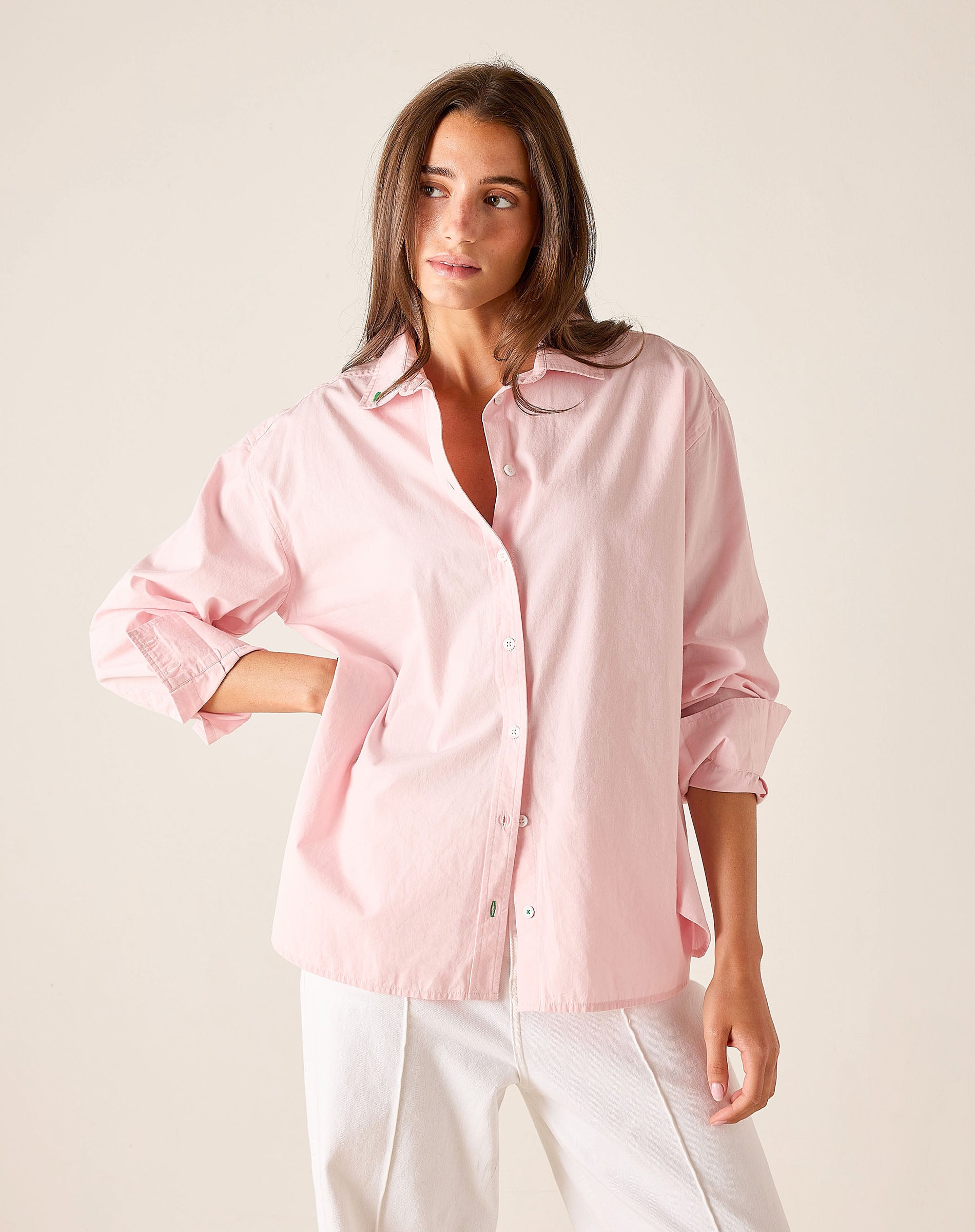 Woman wearing a light pink shirt and white pants against a plain background