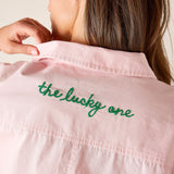 Pink shirt with 'the lucky one' embroidery on a plain background