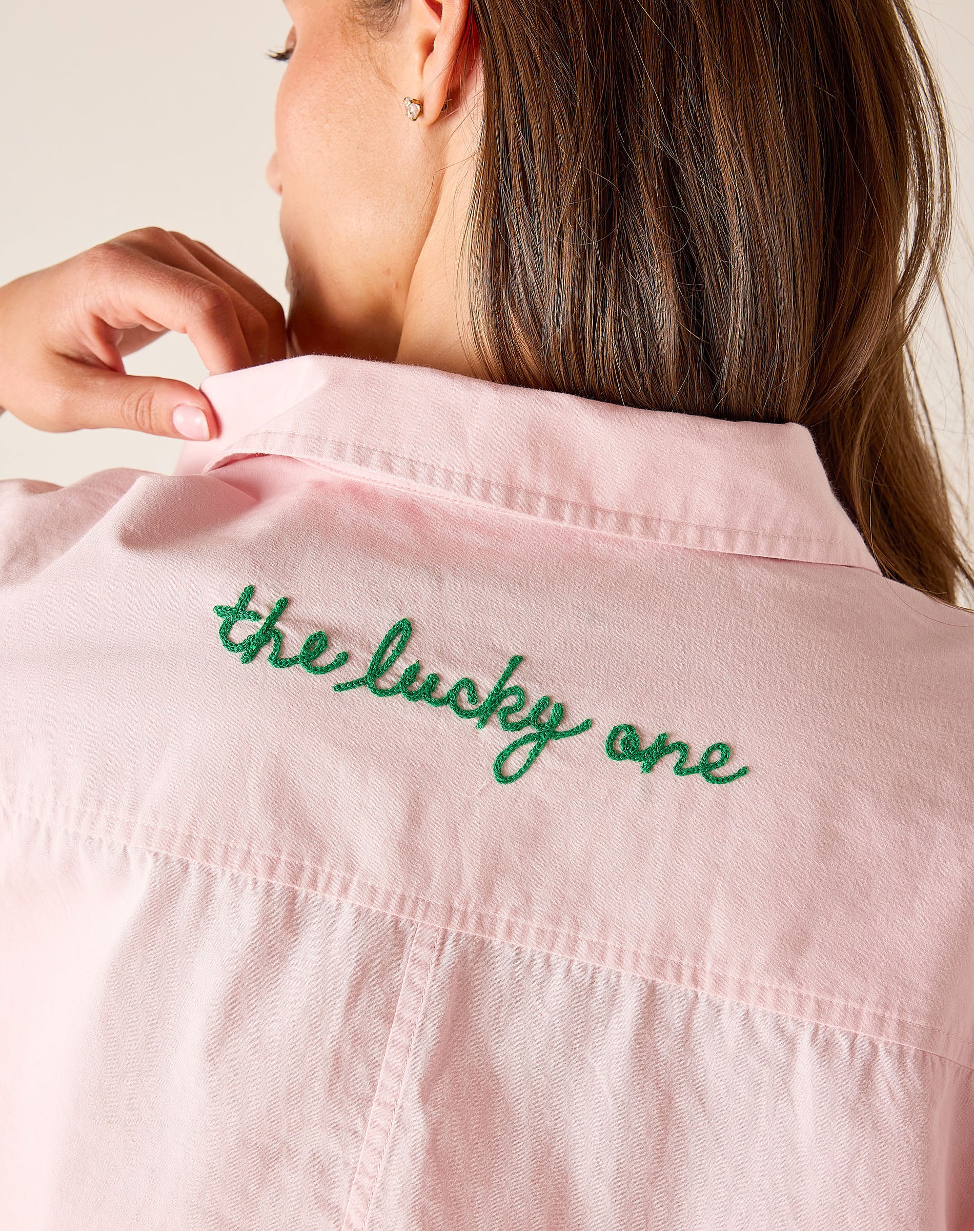 Pink shirt with 'the lucky one' embroidery on a plain background