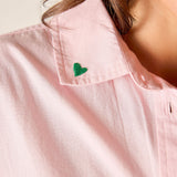Close-up of a pink shirt with a green heart emblem on a plain background