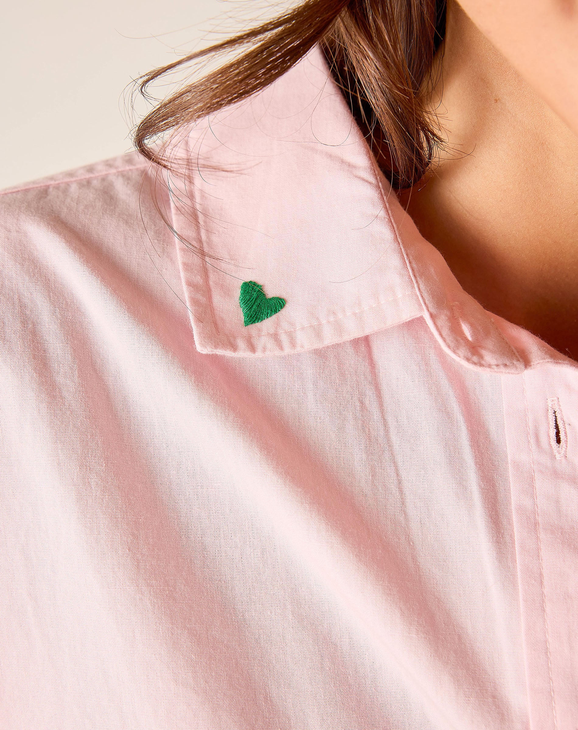 Close-up of a pink shirt with a green heart emblem on a plain background