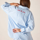 Light blue shirt with 'Sea la vie' text on the back, worn by a person against a beige background