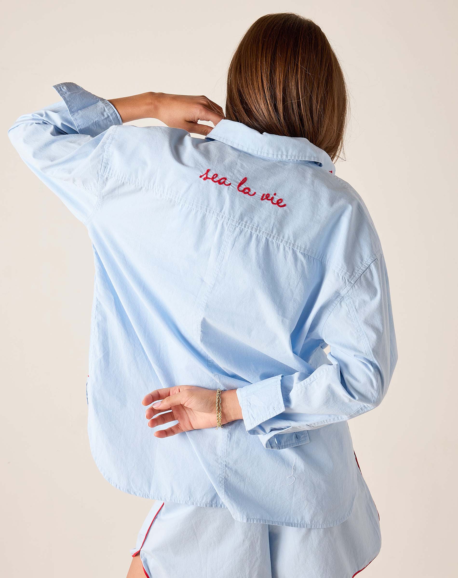 Light blue shirt with 'Sea la vie' text on the back, worn by a person against a beige background