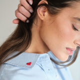 Close-up of a person wearing a clear face mask with a light blue shirt featuring a red heart.