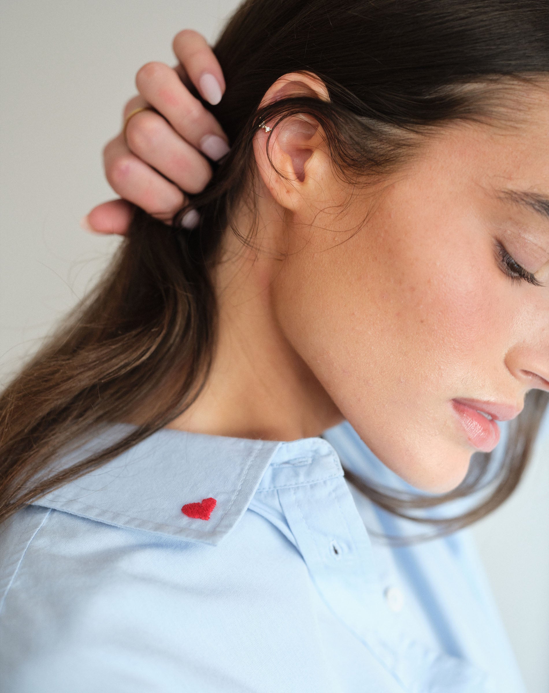 Close-up of a person wearing a clear face mask with a light blue shirt featuring a red heart.