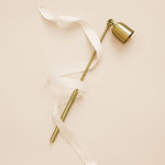 Brass candle snuffer wrapped in white ribbon engraved with 'up to snuff'.