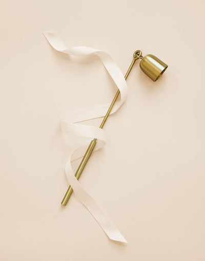 Brass candle snuffer wrapped in white ribbon engraved with 'up to snuff'.