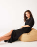 woman showcasing black mersea breezy light kaftan dress lounging on puff seat