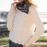 Natural color cable knit sweater with a thick, textured weave and decorative scalloped hem.