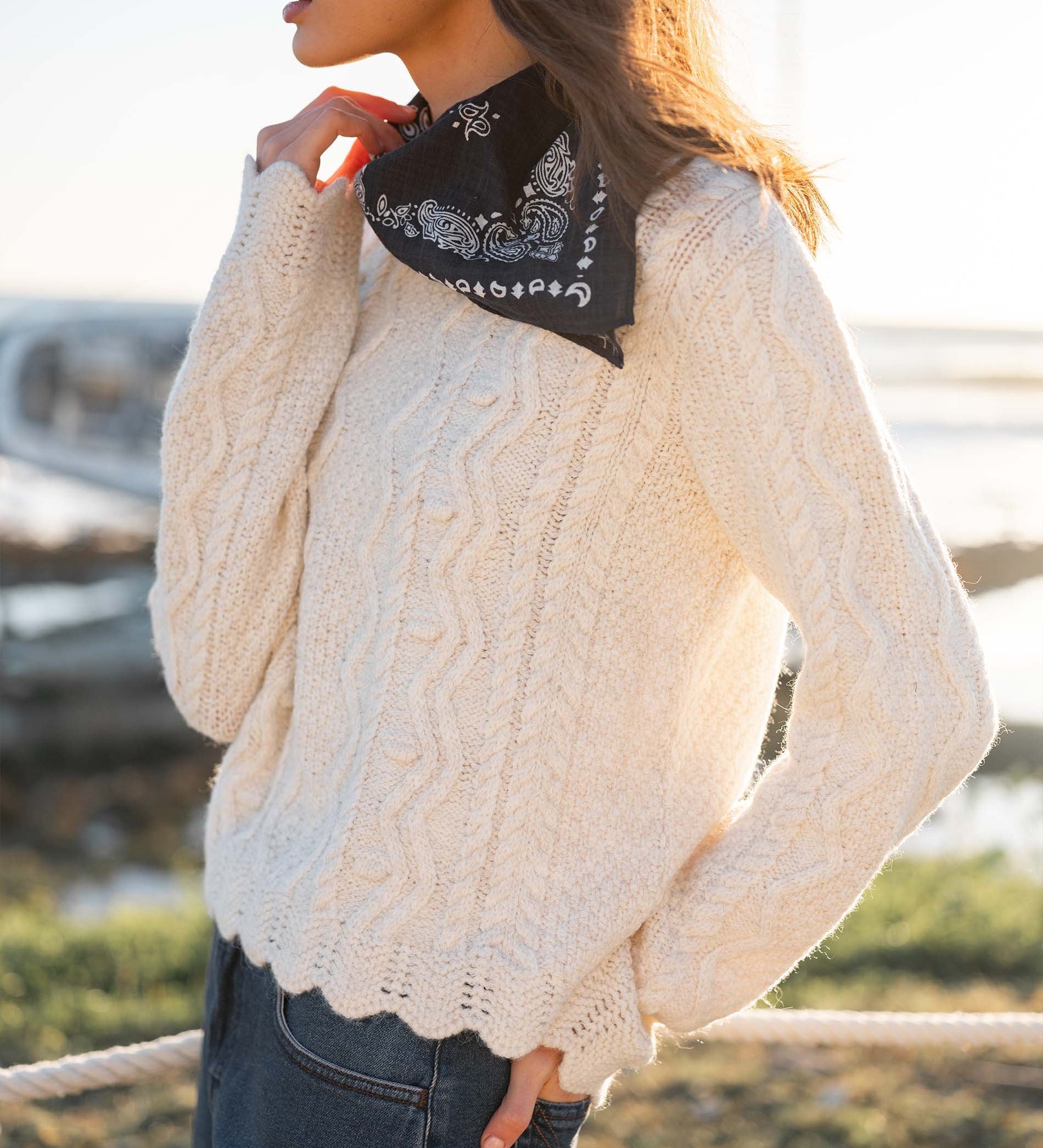 Natural color cable knit sweater with a thick, textured weave and decorative scalloped hem.