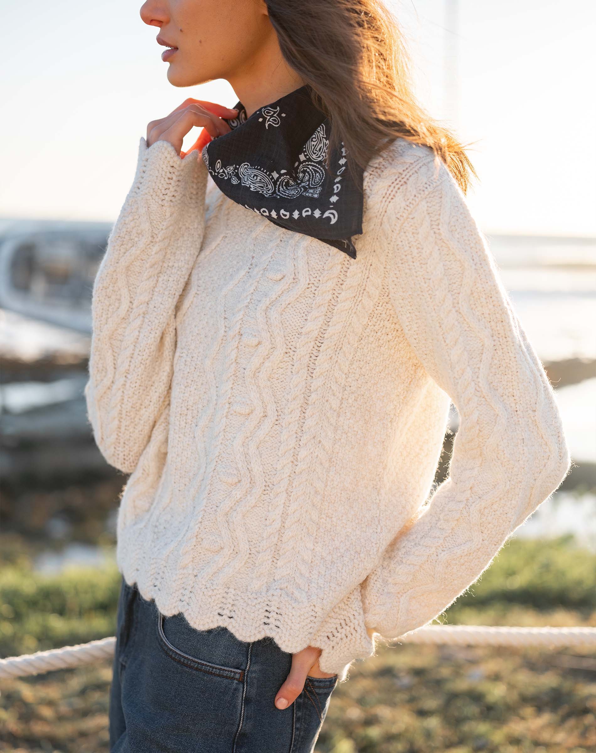 Natural color cable knit sweater with a thick, textured weave and decorative scalloped hem.