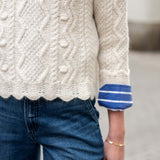 Natural knit cable-stitch sweater with a striped blue and white cuff.