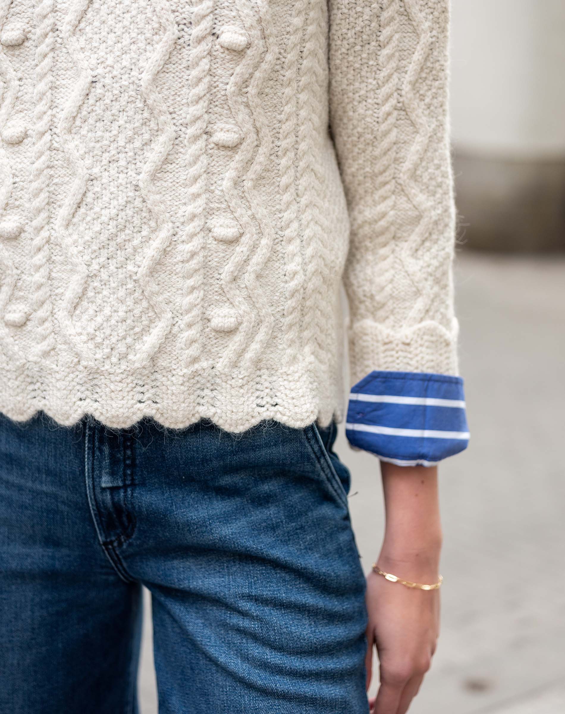Natural knit cable-stitch sweater with a striped blue and white cuff.