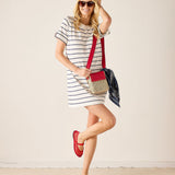 Woman in a striped dress with red shoes and a red bag against a plain background