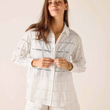 Woman wearing a white embroidered shirt and shorts set against a plain background