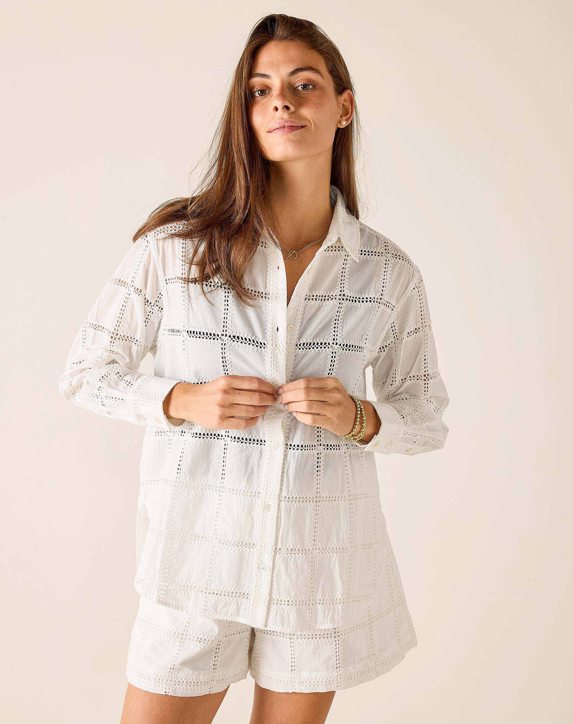 Woman wearing a white embroidered shirt and shorts set against a plain background