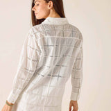 Woman wearing a white lace shirt and shorts against a plain background
