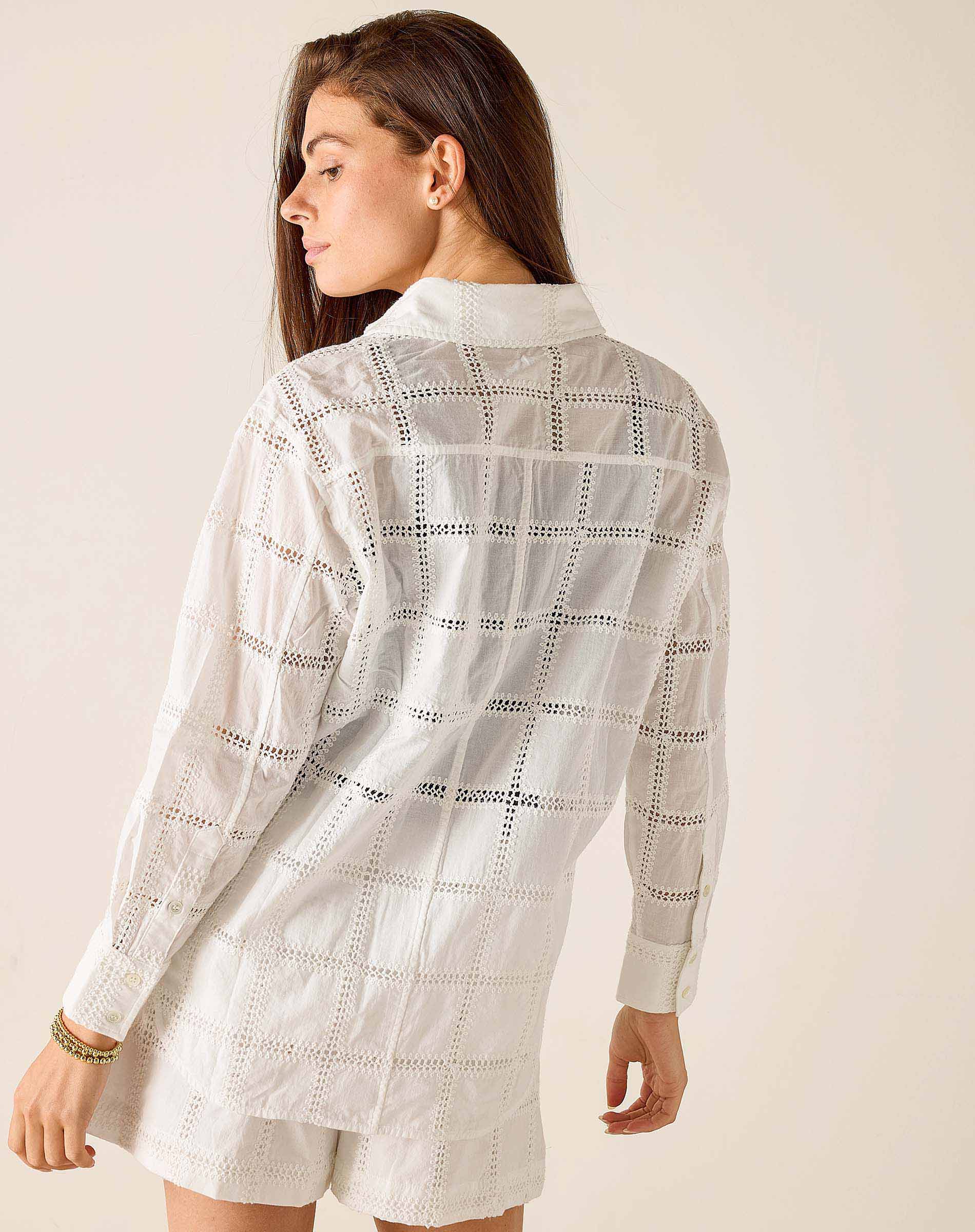 Woman wearing a white lace shirt and shorts against a plain background