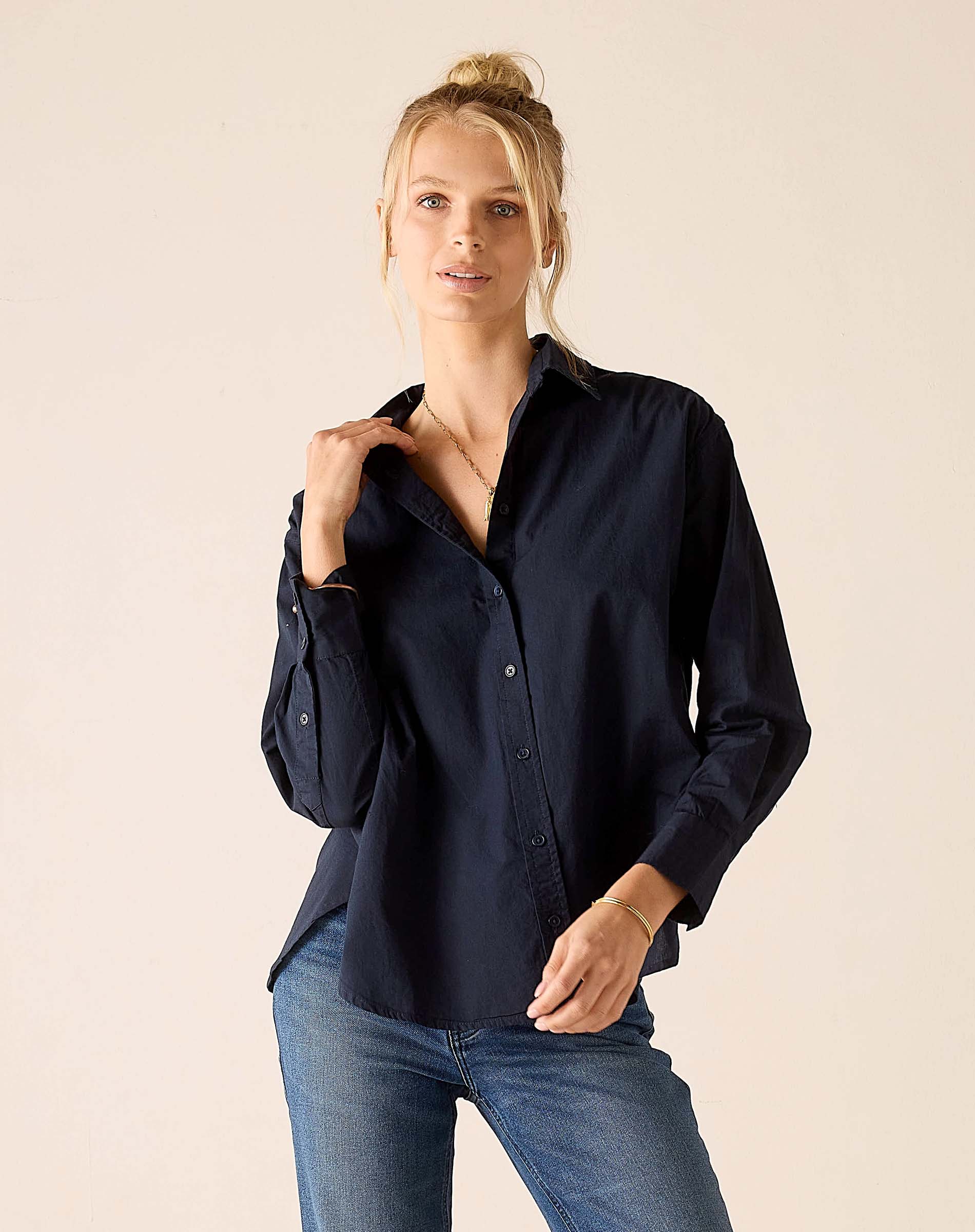 Woman wearing a navy blue shirt and blue jeans against a beige background