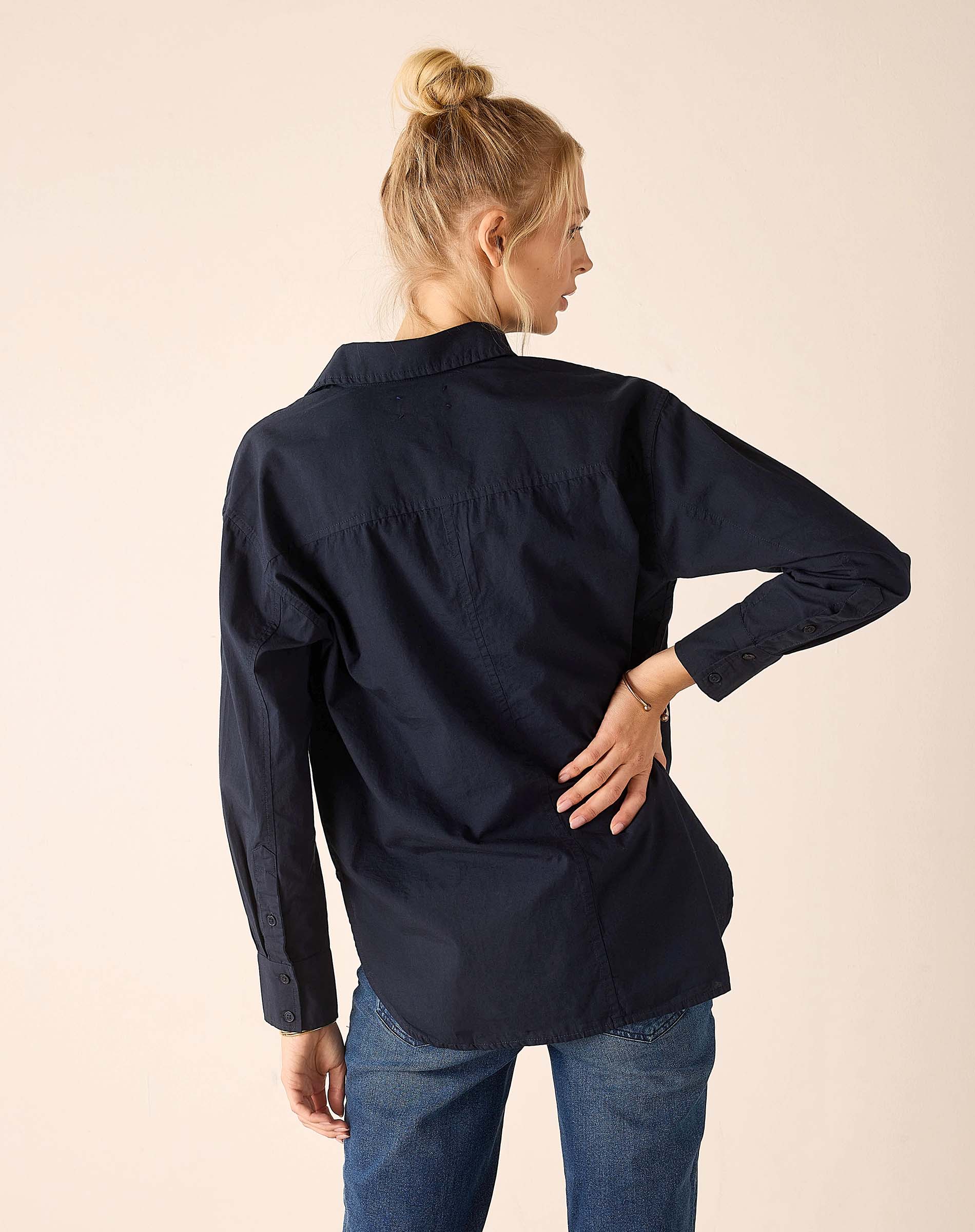 Person wearing a navy blue shirt and blue jeans on a beige background