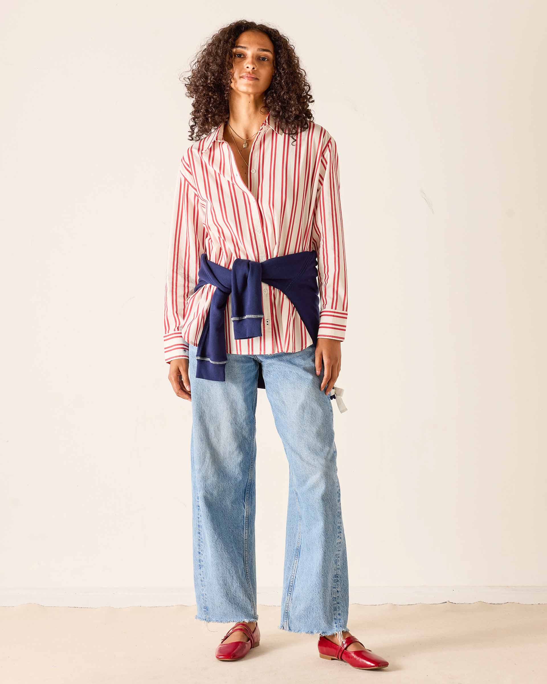 Woman wearing a striped shirt with a belt and jeans on a plain background