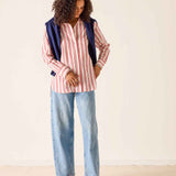 Woman wearing a striped shirt, blue jeans, and red shoes against a plain background