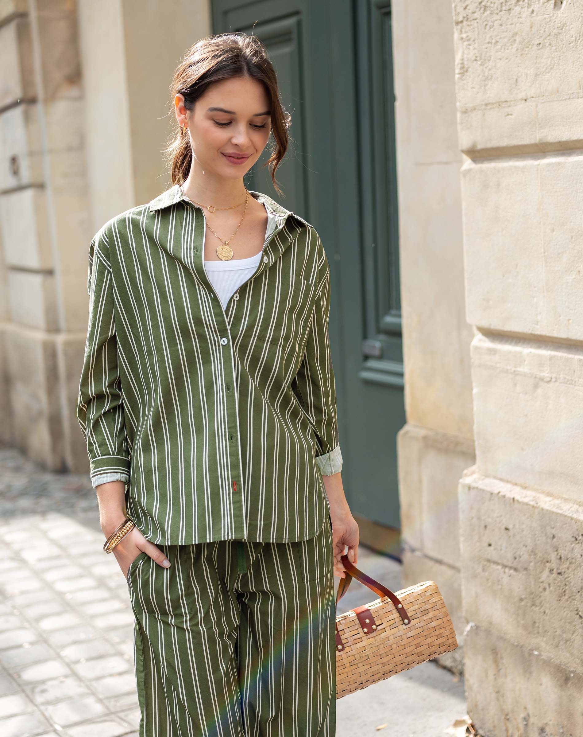 Woman in green striped outfit holding a straw bag against a building background