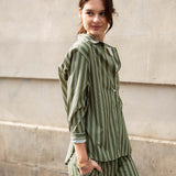 Woman wearing a green and white striped outfit standing against a light-colored wall.