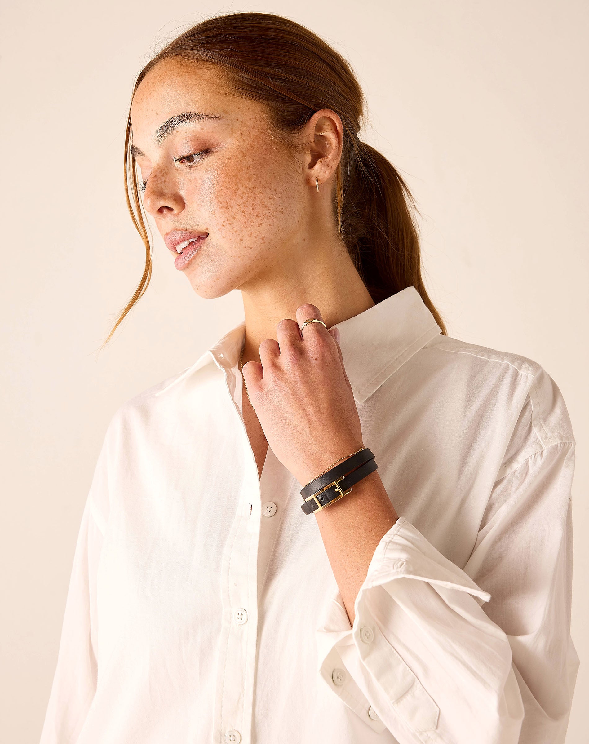 Woman wearing a white shirt and black bracelet on a beige background