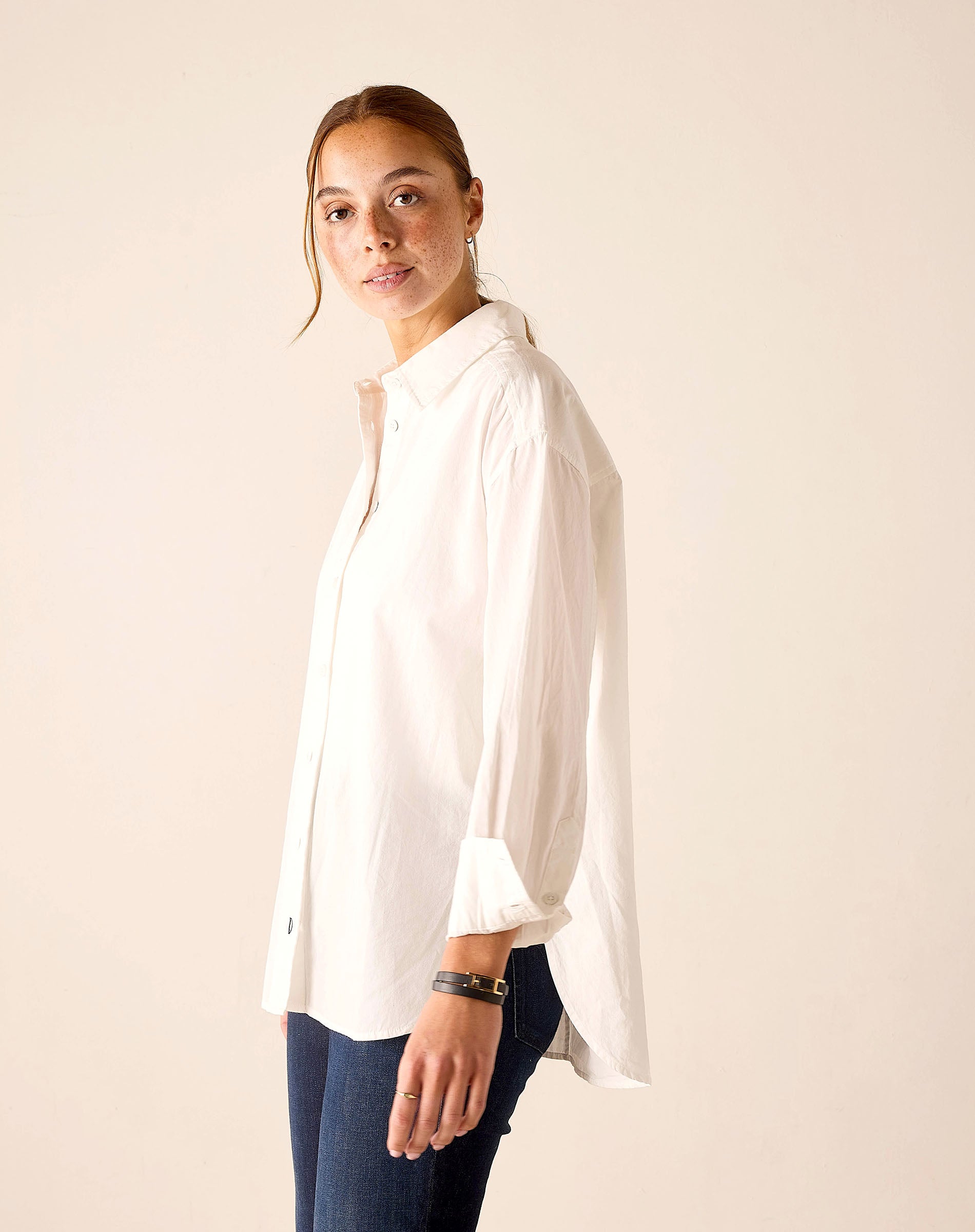 Woman wearing a white shirt and blue pants against a plain background