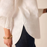 Person wearing a white blouse with balloon sleeves and dark jeans on a neutral background