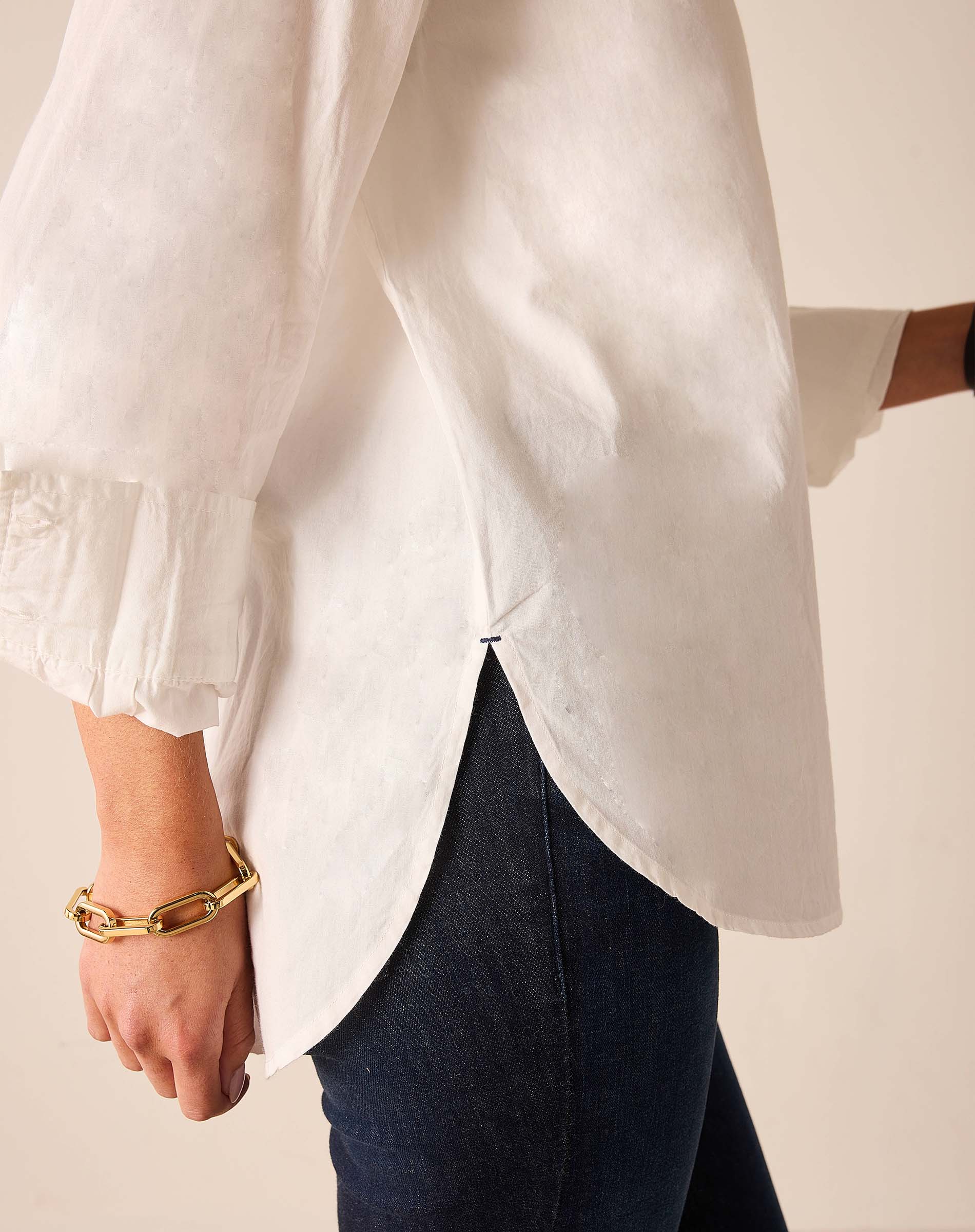 Person wearing a white blouse with balloon sleeves and dark jeans on a neutral background